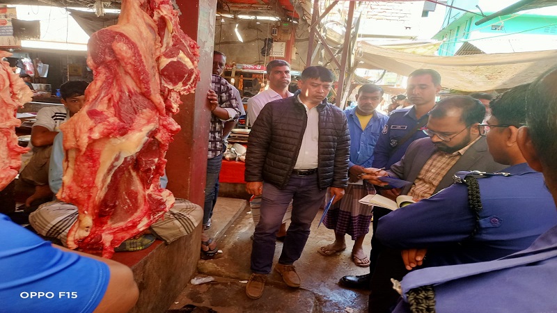 কাপ্তাই নতুনবাজারে ভোক্তা-অধিকার সংরক্ষণ অধিদপ্তরের সহকারী পরিচালক রানা দেবনাথ একটি মাংসের দোকানে মূল্য তালিকা যাচাই করছেন এবং পুলিশ সদস্যরা পাশে দাঁড়িয়ে আছেন।