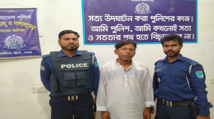 A man in civilian clothes, identified as GM Jewel Mia, being escorted by police officers during a night operation in Ashulia.