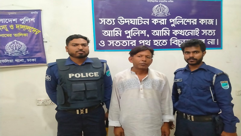A man in civilian clothes, identified as GM Jewel Mia, being escorted by police officers during a night operation in Ashulia.